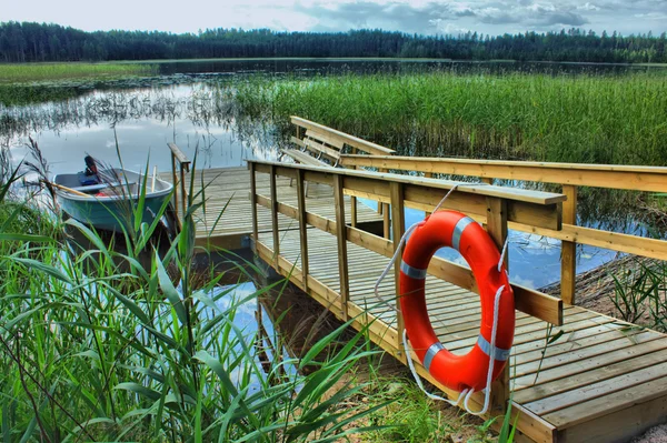 Лодка с деревянным пирсом с спасательным кругом на озере — стоковое фото