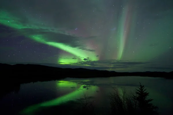 Звезды и северное сияние над темной дорогой на озере — стоковое фото