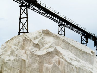 Pile of sea salt under conveyor of saline refinery clipart