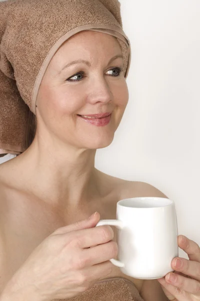 Mujer con una toalla en la cabeza sosteniendo una taza en sus manos . — Foto de Stock