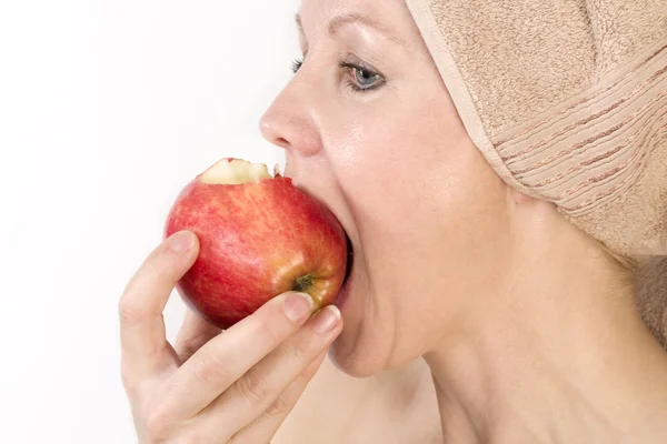 Adult woman with a towel on her head biting an apple. — Stock Photo, Image