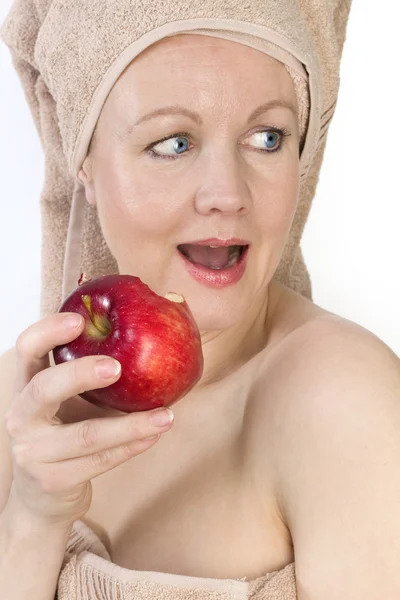 Femme adulte avec une serviette sur la tête mordant une pomme . — Photo