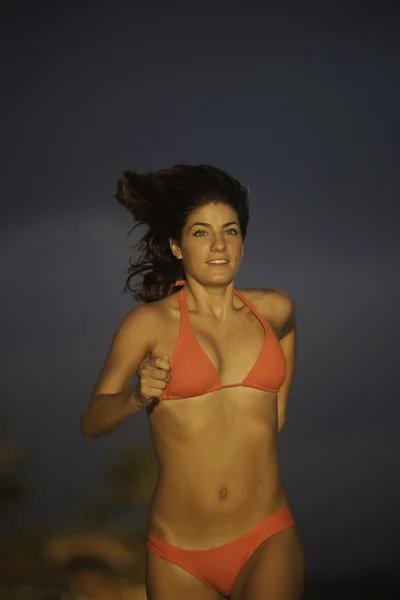 Mladá žena běží na pláži při východu slunce — Stock fotografie