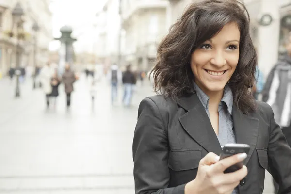 Молодая женщина с улыбкой и смартфоном ходит по улице — стоковое фото