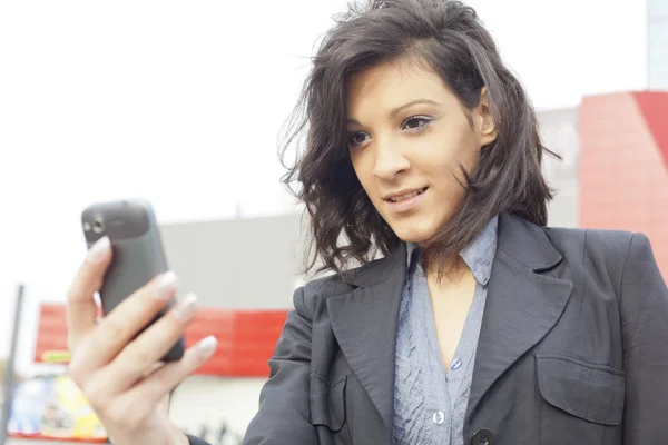Jonge vrouw met mobiele telefoon wandelen, blured zakelijke gebouw in — Stockfoto