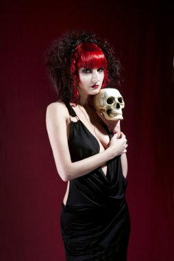 Studio portrait of young pale woman in black dress holding skull clipart