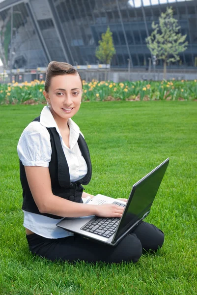 Молодая женщина сидит на газоне с ноутбуком — стоковое фото