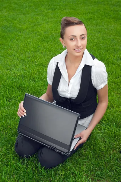 Ung kvinna sitter på gräsmattan med laptop — Stockfoto