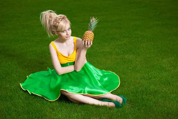 Flicka med ananas som sitter på gräsmattan — Stockfoto