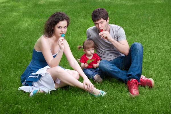Família feliz com a filha sentada na grama verde no parque — Fotografia de Stock