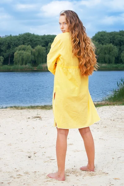 Giovane donna attraente dai capelli lunghi in abito giallo sulla spiaggia del fiume — Foto Stock