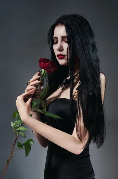 Hübsche, brünette Frau im schwarzen Kleid mit roter Rose — Stockfoto
