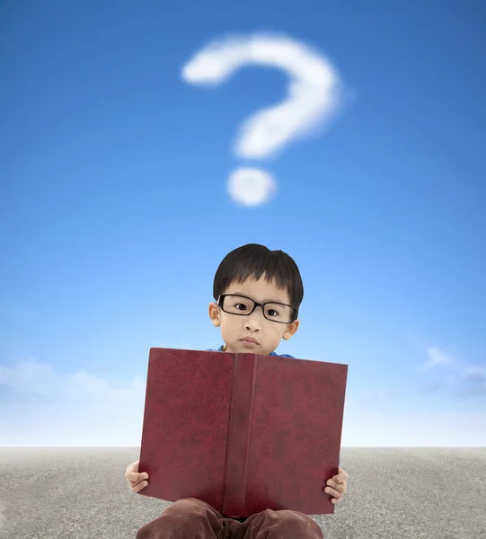 Μικρό αγόρι που κατέχουν το βιβλίο και το αγγλικό ερωτηματικό σύννεφο φόντο — Φωτογραφία Αρχείου