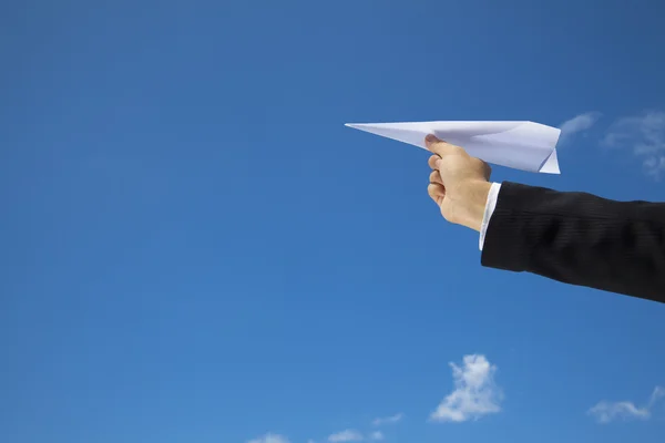 Hand of Businessman letting an airplane made of paper fly over blue sky — Stock Photo, Image