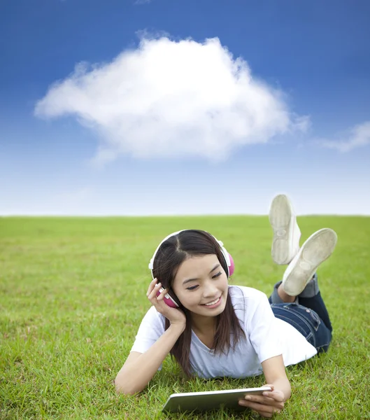 Chica feliz usando el ordenador táctil con auriculares en el prado —  Fotos de Stock