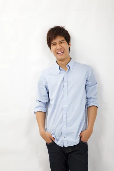 Счастливый улыбающийся азиатский молодой человек, прислонившийся к белой стене — стоковое фото