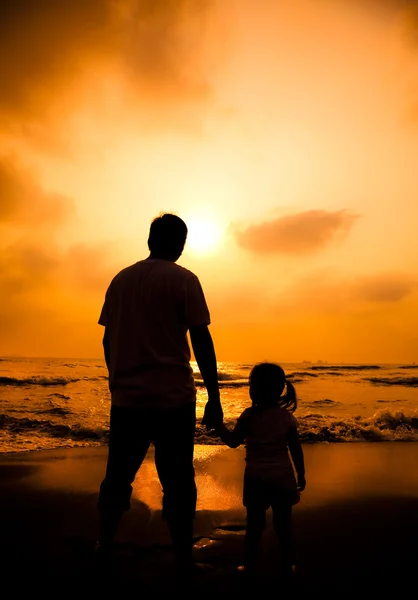 La silueta del padre sosteniendo la mano de la niña en la playa — Foto de Stock