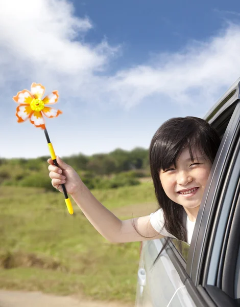 Niña feliz sosteniendo molino de viento en el coche — Foto de Stock