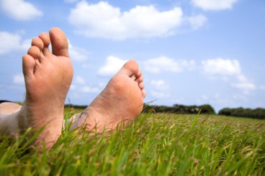 Relaxed foot on grass with cloud background clipart