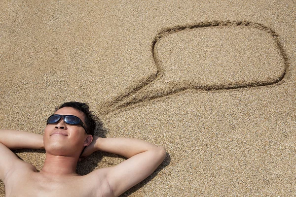 Usmívající se mladý muž leží na pláži a dialogové okno symbol — Stock fotografie