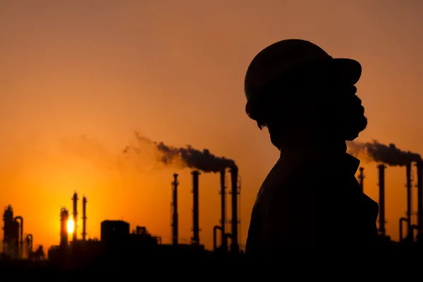 Die Silhouette eines Arbeiters in einer Ölraffinerie bei Sonnenuntergang — Stockfoto