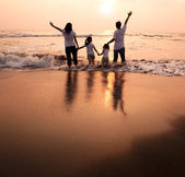 glückliche Familie Händchen haltend am Strand und den Sonnenuntergang beobachtend