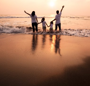 Happy family holding hands on beach and watching the sunset clipart