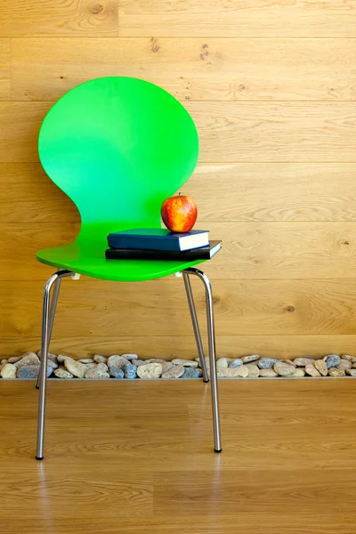 Cadeira verde, maçã vermelha e alguns livros contra parede / modo de madeira — Fotografia de Stock