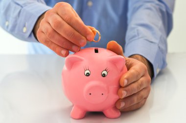 Man putting wedding ring into a piggy bank. clipart