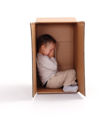 Sad little boy hiding in cardboard box clipart