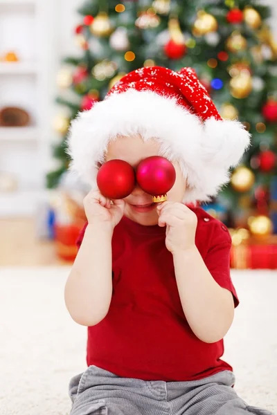Menino segurando decoração de Natal na frente dos olhos — Fotografia de Stock