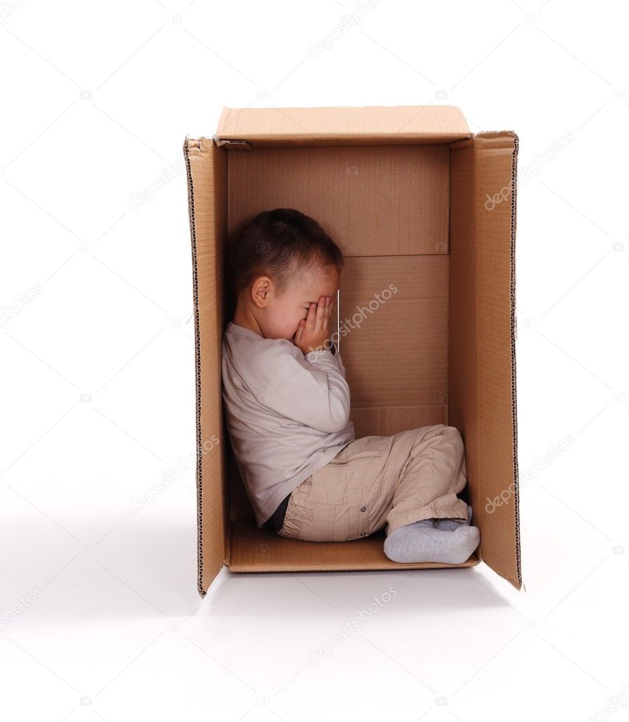 Sad little boy hiding in cardboard box