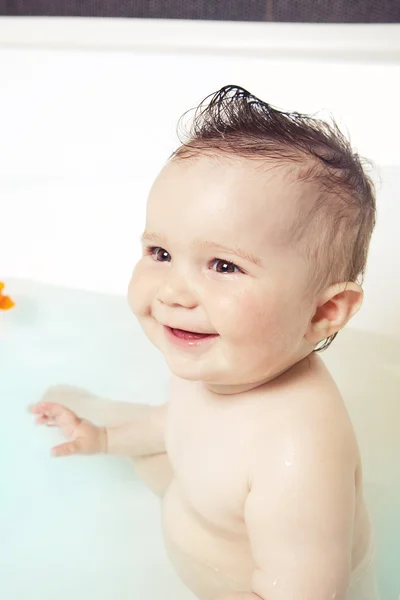 Симпатичный ребенок, сидящий в воде, веселящийся и улыбающийся во время принятия ванны — стоковое фото