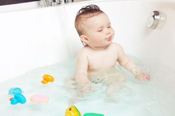 Bebê bonito brincando com água e mostrando língua enquanto toma banho — Fotografia de Stock