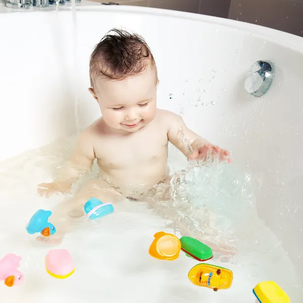 Lindo bebé sonriente divirtiéndose y salpicando agua mientras toma un baño —  Fotos de Stock
