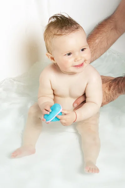 Lindo bebé sostenido por las manos del padre, jugando con un juguete de goma y sonriendo mientras toma un baño —  Fotos de Stock