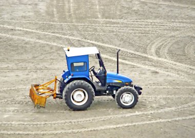 Sahil kumu temizlemeyi bekleyen mavi Greyder traktör