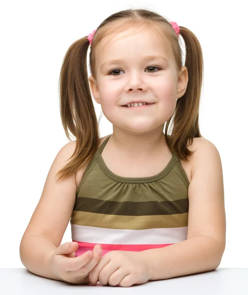 Glückliches kleines Mädchen sitzt an einem Tisch und lächelt — Stockfoto