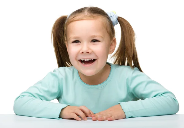 Счастливая маленькая девочка сидит за столом и улыбается — стоковое фото