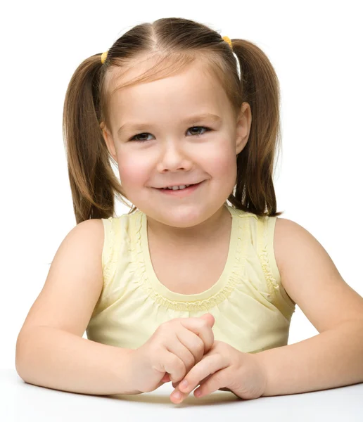 Joyeux petite fille assise à une table et sourire — Photo