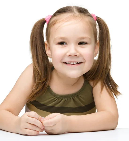 Ευτυχισμένη κοριτσάκι που κάθεται σε ένα τραπέζι και το χαμόγελο — Φωτογραφία Αρχείου