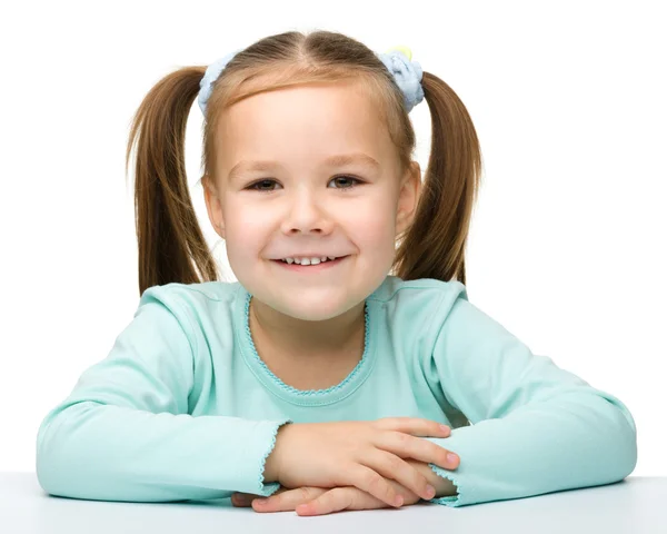Bir tablo ve bir gülümseme mutlu küçük kız oturuyor — Stok fotoğraf