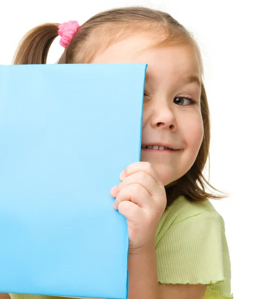 Cute little girl is hiding behind a book — Stock Photo, Image