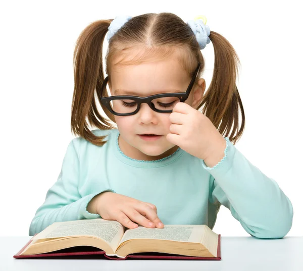 Klein meisje leest een boek terwijl het dragen van een bril — Stockfoto