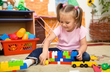 Little girl is playing with building bricks clipart