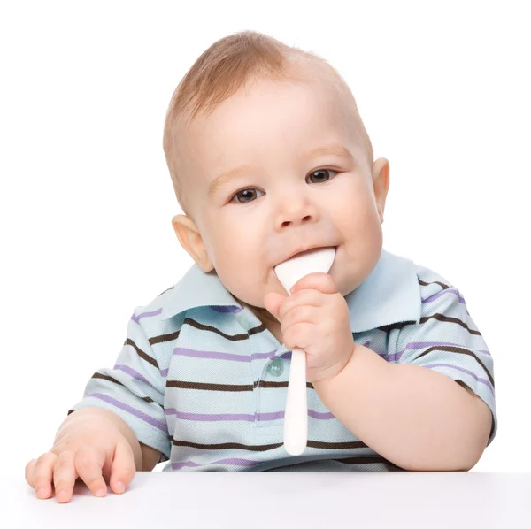 小男孩在咬一把勺子，坐在桌 — 图库照片