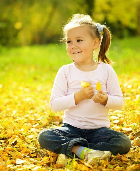 Menina bonito está brincando com folhas no parque — Fotografia de Stock