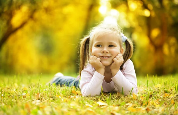 Schattig klein meisje speelt met bladeren in park — Stockfoto