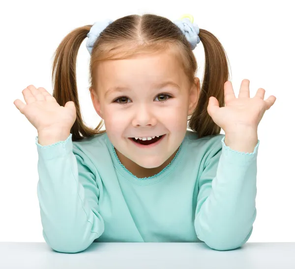 Glad liten flicka sitter vid ett bord och leende — Stockfoto