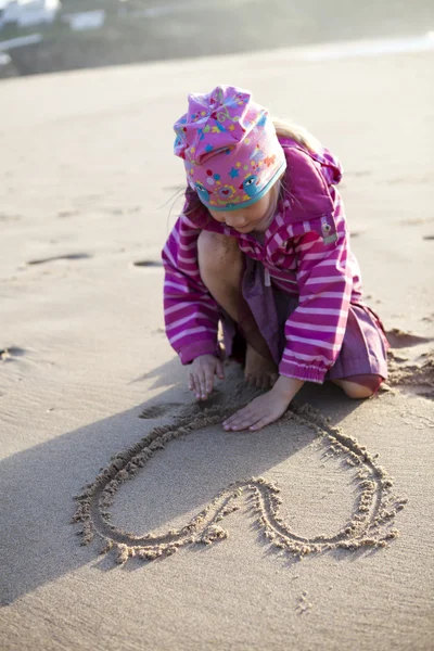 Girl drawing a heart in sand — Stock Photo, Image